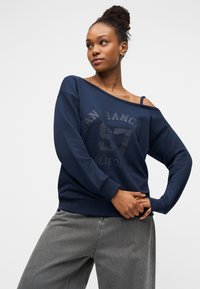 Επανωφόρι σε σκούρο μπλε ναυτικό χρώμα με σχεδιασμό που αφήνει τους ώμους ακάλυπτους, με το τυπωμένο κείμενο «SAN FRANCISCO 97 CALIFORNIA» σε φθαρμένο στυλ και ριμπ μανσέτες.