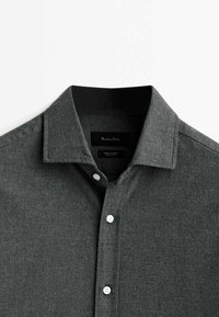 Chemise gris foncé à boutons avec col pointu, trois boutons blancs visibles et doublure intérieure noire du col sur fond blanc.