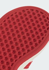 Červená gumová podrážka s včelí pláství vzorem, s bílým okrajem. Texturovaný povrch zvyšuje přilnavost a odolnost.