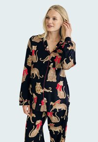 Pajama set in black fabric featuring leopard patterns with red ribbons and holly accents. Long sleeves, button-up shirt, and matching pants.