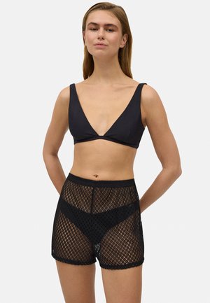 Bralette negra con un escote en V profundo y tirantes anchos, combinada con shorts negros de tiro alto hechos de tejido de malla con un patrón de diamantes.