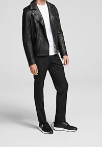 Svart lädermotorcykeljacka, vit t-shirt, skräddarsydda svarta byxor och svarta sneakers med vita sulor. Slät textur och åtsittande design.