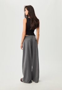 Czarny bezrękawnik połączony z szarymi spodniami o wysokim stanie i szerokich nogawkach, wyposażonymi w dwie tylne kieszenie. Gładki materiał o luźnym kroju.