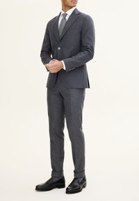 Completo di lana grigio con rever a punta, bottone singolo e vestibilità su misura; abbinato a una cravatta grigio chiaro e scarpe in pelle nere.