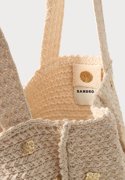 Μπεζ τσάντα γάντζου με πλατιές τιράντες, χρυσά διακοσμητικά κουμπιά και μαγνητικό κλείσιμο με ετικέτα Sandro στο εσωτερικό.