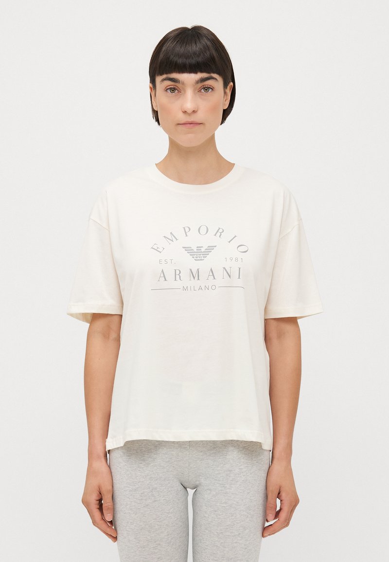 Bijela, oversized pamučna majica s kratkim rukavima. Sadrži sivi logo natpis "EMPORIO ARMANI MILANO" i okrugli izrez.