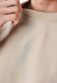 Beige katoenen sweatshirt met een geribde kraag en geborduurd "Project x Paris" logo in het wit, dat een subtiele textuur benadrukt.