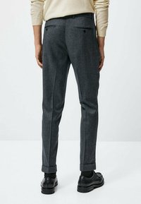 Graue Wollhose mit schmaler Passform, ausgestattet mit zwei Gesäßtaschen und Umschlägen. Kombiniert mit schwarzen Schuhen für einen formellen Look.