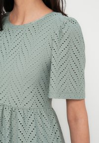 Jasnozielona sukienka z wzorem w jodełkę, z wycięciami, krótkimi bufkami i marszczoną talią.