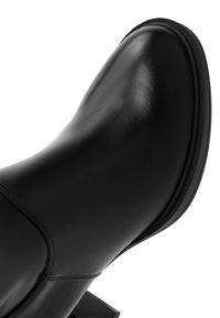 Botín de cuero negro con un acabado liso, punta redonda, costuras mínimas y un tacón bajo y resistente. La suela tiene una elevación sutil.