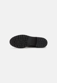 Semelle de chaussure en caoutchouc noir avec un motif de semelle texturé, comportant des rainures profondes pour l'adhérence et la durabilité. Pas de marquage visible sur le talon.