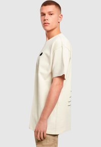 Kremfarget oversized t-skjorte laget av bomull, med et grafisk trykk på venstre bryst og en avslappet passform.