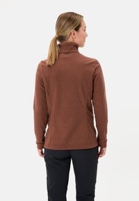 Giacca in pile marrone con colletto alto, texture liscia, design aderente e dettagli di cucitura discreti sull'orlo e sulle maniche.