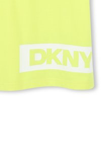 Camiseta de algodón amarilla con un gran logo blanco "DKNY" en el dobladillo. La tela es suave, con un ligero brillo y un corte relajado.