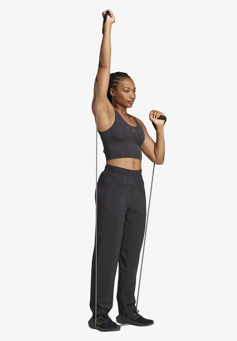 Top deportivo negro y pantalones de chándal negros sueltos, sosteniendo bandas de resistencia mientras está de pie. Texturas suaves con una silueta ajustada.