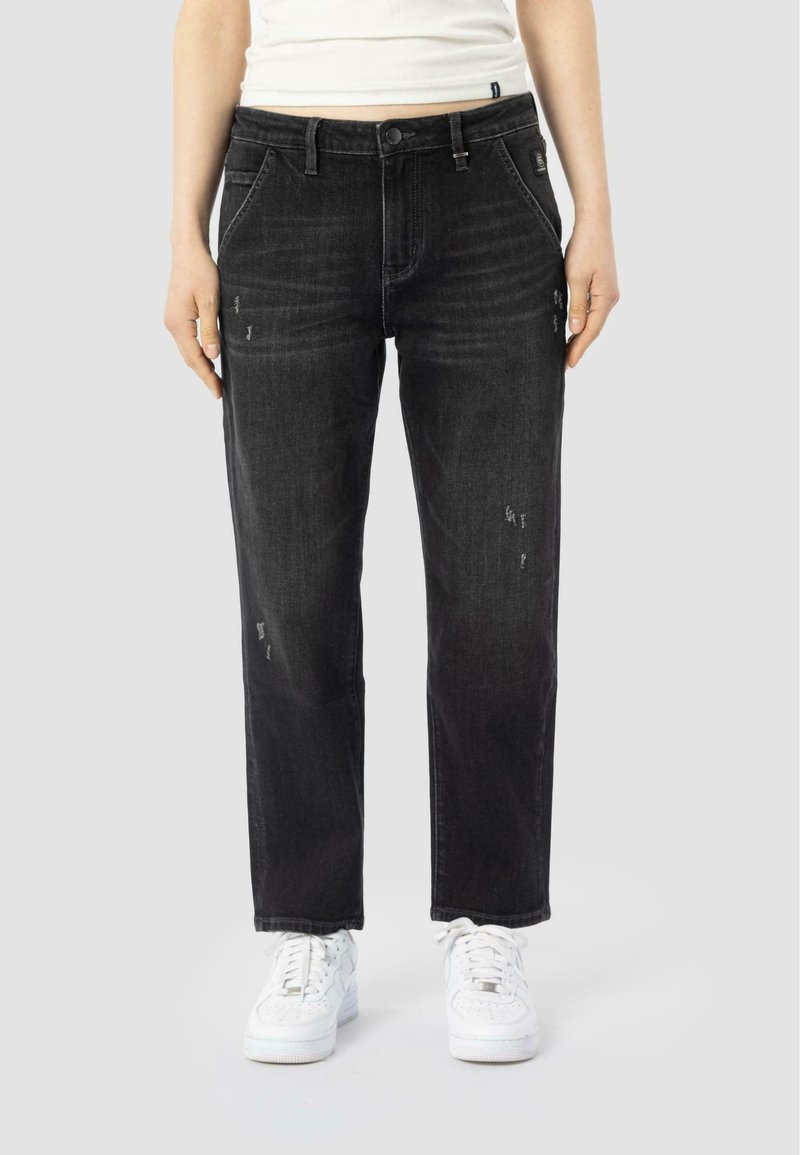 Jeans de mezclilla negra con un corte relajado, que presentan detalles desgastados, cinco bolsillos y cierre de botón, combinados con zapatillas blancas.