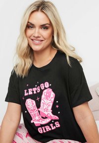 Svart bomullströja med rosa grafik av cowboystövlar och texten "LÅT OSS GÅ TJEJER," mot en vit bakgrund. Korta ärmar.