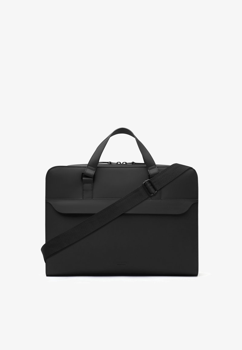 Mallette rectangulaire noire avec deux poignées, une poche à rabat à l'avant et une bandoulière réglable traversant le devant, sur fond blanc.