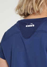 Navy blue athletic shirt with a rounded neckline, featuring a logo at the back, made from a smooth, lightweight fabric.