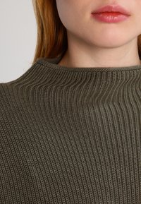 Maglione verde oliva a collo alto, lavorato a maglia con texture a costine, caratterizzato da un design aderente e una finitura liscia.