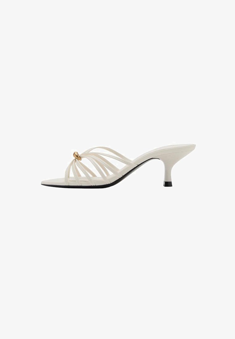 Sandales à talons blancs à lanières avec un design courbé, dotées d'une accent en or et d'une semelle noire. Texture lisse et style ouvert.
