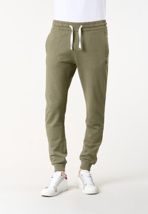 Pantaloni jogger verde oliva con vita elasticizzata e coulisse bianche indossati con scarpe da ginnastica basse bianche su modello.