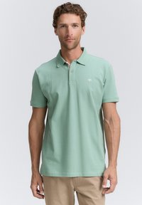 Mintgrøn polo shirt lavet af bomuld med krave, to knapper og et lille logo på brystet. Korte ærmer og lige kant.