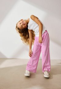 Hvid ærmeløs top kombineret med bukser i pink og hvid gingham-rute. Bukserne er løstsiddende med en elastisk talje og en subtil tekstur.