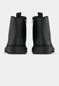 Botine negre, realizate din piele netedă, cu un fermoar pe spate, o buclă pentru a fi trase și o talpă texturată robustă.