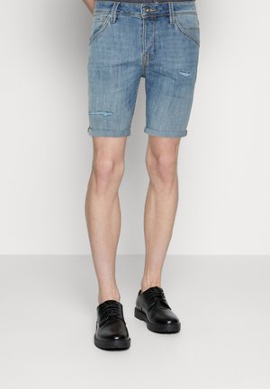 Pantalones cortos de denim en azul claro con un diseño desgastado; con puños enrollados, bolsillos estándar y acompañados de zapatos negros con cordones.
