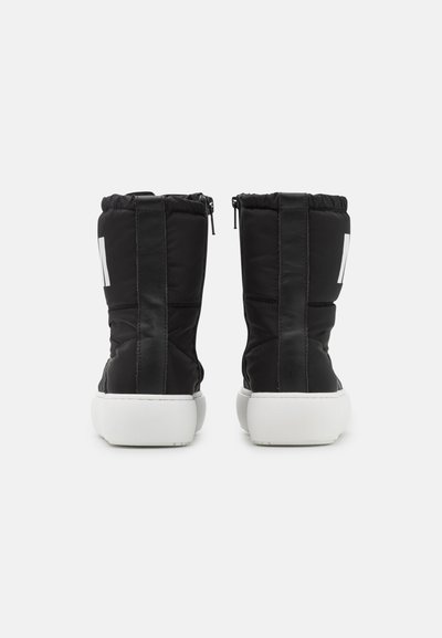 Botas pretas acolchoadas com canos altos, fechos de zipper e solas de borracha brancas. Apresentam uma textura acolchoada e detalhes em painéis laterais.