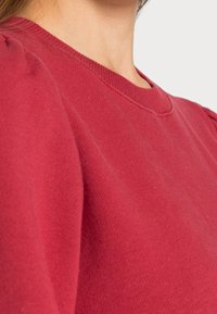 Roter Pullover mit Rundhalsausschnitt und Puffärmeln, aus weichem Baumwollstoff gefertigt. Verfügt über gerippte Bündchen und Halsausschnitt.
