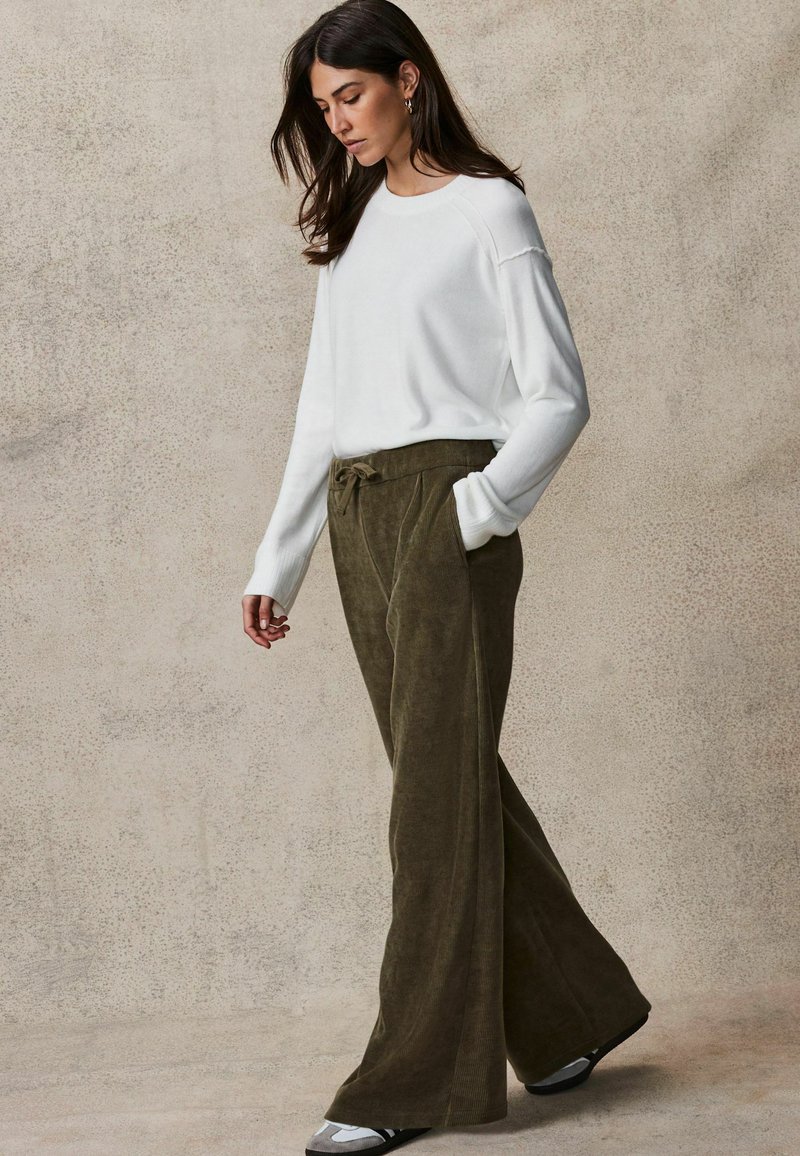 Maglione bianco in misto cotone con polsini a coste, abbinato a pantaloni larghi in corduroy verde oliva con vita con coulisse e tasche laterali.