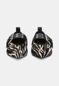 Zapatos slip-on de patrón de cebra en blanco y negro con punta afilada, correa de cuero con tachuelas metálicas y una lengüeta en la parte trasera.