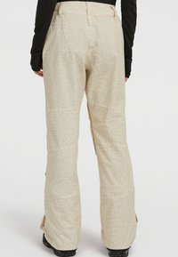 Beige met patroon skibroek met een losse pasvorm, voorzien van een hoge tailleband en ritsen bij de enkels. De textuur is glad met een subtiel patroon.