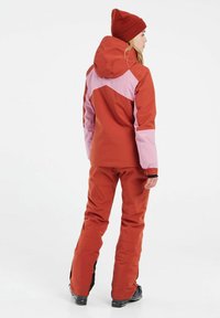 Rode en roze sneeuwjack met capuchon en elastische manchetten, gecombineerd met bijpassende rode broeken. Soepele textuur en aangesloten ontwerp. Geaccentueerd met zwarte details.