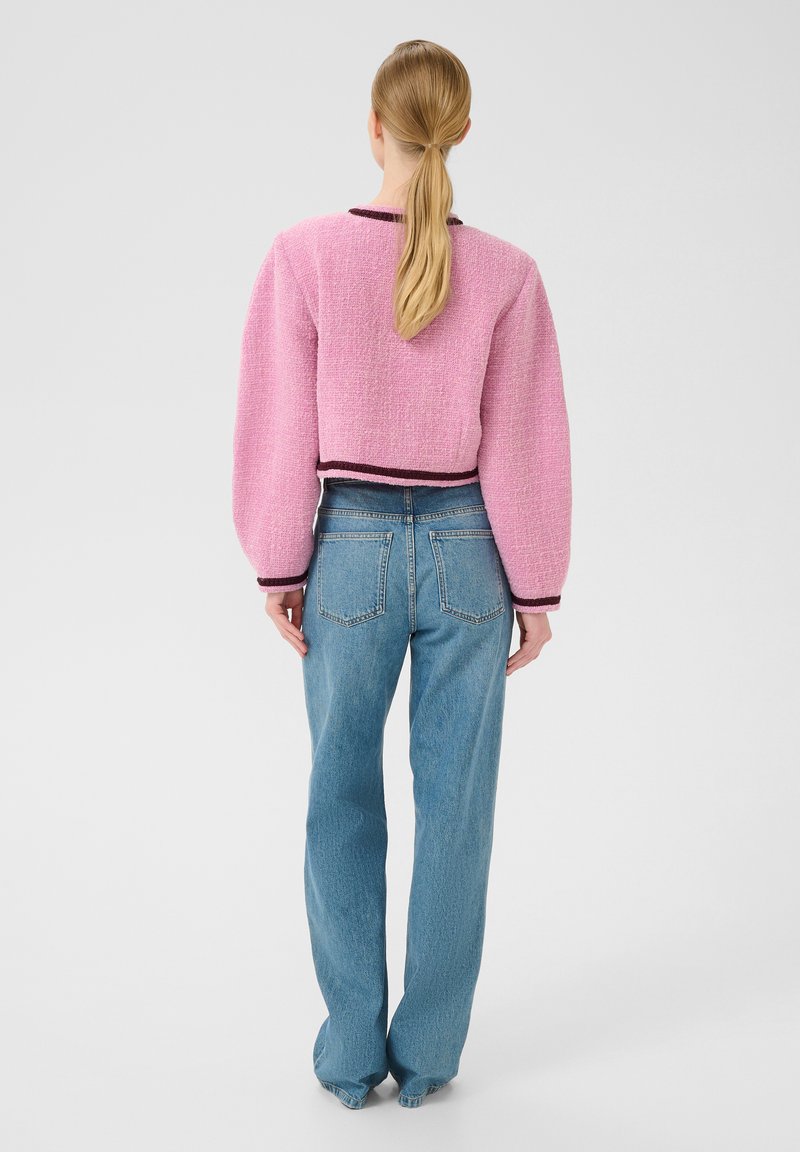 Rosa texturerad kort tröja med puffärmar, svart kant i nederkant, ihop med ljusblå raka jeans, bakvy.