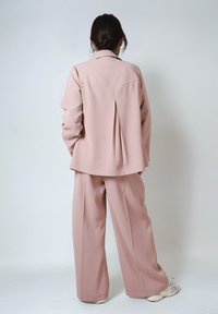 Light pink matching set featuring a tailored blazer with a pleated back and wide-leg trousers, made from smooth fabric with a subtle sheen.