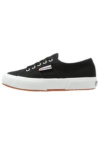 Zapatillas de lona negras con suela de goma blanca, punta redonda y cierre de cordones. Cuenta con una suela texturizada y un parche con el logo en el lateral.
