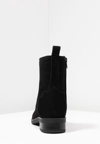 Stivale alla caviglia in suede nero con punta arrotondata, chiusura con zip, linguetta e tacco basso impilato, dotato di suola in gomma testurizzata.