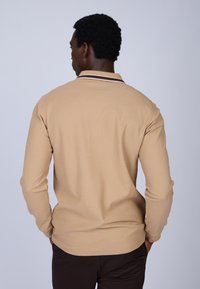 Polaire beige à manches longues avec un col rayé marron et blanc, tissu texturé et coupe ajustée, vue de dos.