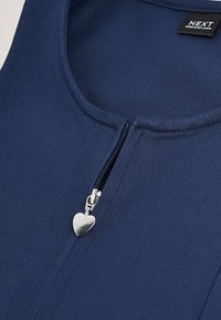 Tessuto blu navy con cursore della cerniera a forma di cuore argentato sotto una scollatura rotonda e un'etichetta nera del marchio Next.
