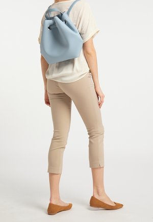 Světle modrý měkký batoh ve tvaru kyblíku s našroubovaným vrškem a stříbrným kováním, nošený s béžovými úzkými kalhotami a hnědými balerínami.