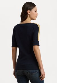 T-shirt marine à manches courtes retroussées. Accents latéraux dans une teinte plus claire. Texture lisse et design ajusté, adapté pour un usage décontracté.
