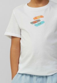 Witte katoenen t-shirt met opgerolde mouwen, versierd met drie kleurrijke skateboardafbeeldingen in oranje, teal en bruin, met het woord "SLVR."