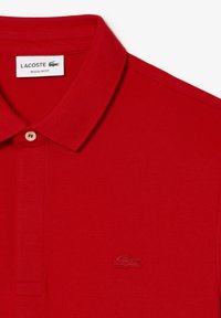 Röd polo skjorta i texturerad bomull, med en klassisk krage, två knappar och en broderad logotyp på vänster bröst. Regular fit.