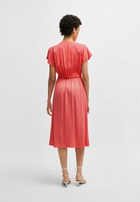 Coral satin midi dress with short flutter sleeves, elastic waist, and a smooth sheen. Features a pleated back and falls to mid-calf.