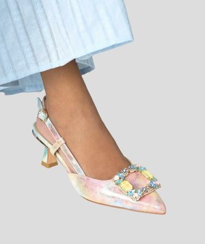 Pie con un tacón de punta y pulsera trasera en rosa pastel, adornado con una hebilla cuadrada decorada con piedras preciosas multicolores.