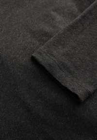 Mörkgrå bomullströja som visar en närbild av tygtexturen, med en synlig fåll och ärmdetalj, med en mjuk, något sliten framtoning.