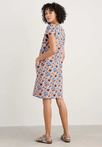 Ziedu kleita ar spilgti oranžu un zilu ziedu rakstu, īsām piedurknēm, līdz ceļiem, ar sānu kabatām un brīvu piegriezumu.